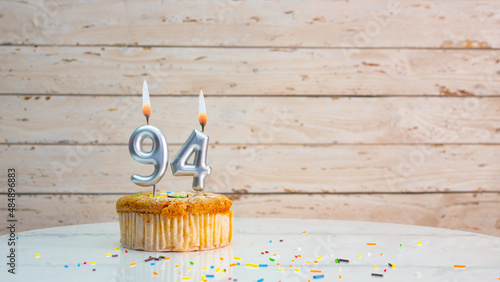 94 year happy birthday greetings from silver numbers on white boards background copy space. Beautiful birthday card with a cupcake with a lit candle for ninety-four years