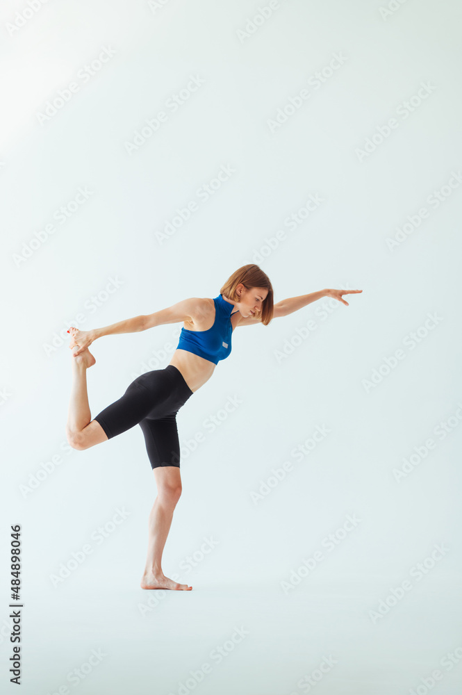 Athletic lady in a blue top and shorts doing stretching on a white background with a serious face. The woman is training. isolated.