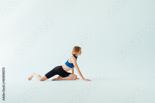 Athletic woman warms up before training on a white background, looks to the side while kneeling.