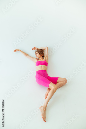 Athletic lady in sporty pink clothes lies on the ground on a white background and looks to the side.