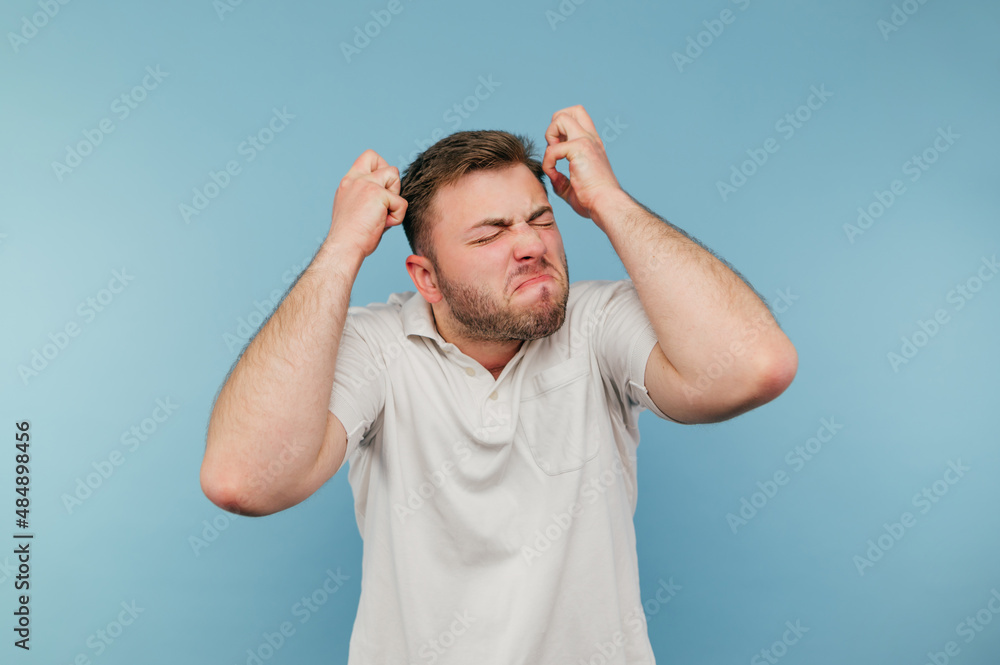 Angry man with bristles in despair isolated blue background wearing white t-shirt. Angry man nervous on the background of the wall Angry man with bristles in despair isolated blue background wearing white t-shirt. Angry man nervous on the background of the wall