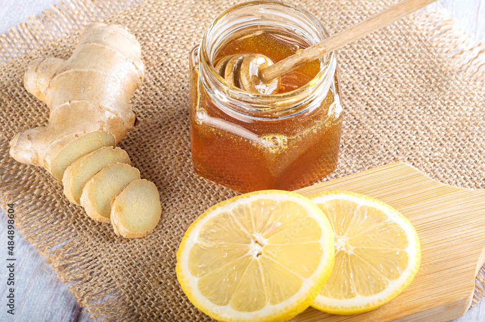 Honey in a glass jar with a spoon for honey. Fresh chopped ginger and lemon slice on burlap. Top view Honey in a glass jar with a spoon for honey. Fresh chopped ginger and lemon slice on burlap. Top view