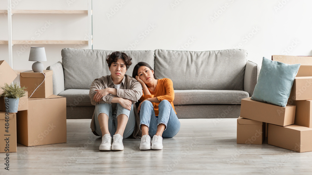Tired Asian couple sitting on floor among carton boxes, looking at camera, feeling exhausted from moving to new home Tired Asian couple sitting on floor among carton boxes, looking at camera, feeling exhausted from moving to new home