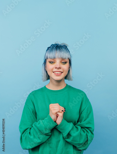 Cute lady in green sweatshirt and colored hair isolated on blue background with smile on face looking at camera.