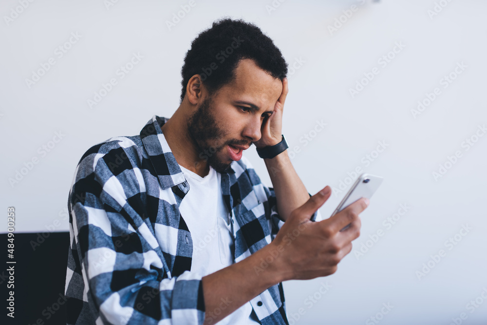 Emotional male employee receive email with bad news feeling shocked in office interior, unhappy hipster guy using smartphone for making online banking solving problems with internet connection Emotional male employee receive email with bad news feeling shocked in office interior, unhappy hipster guy using smartphone for making online banking solving problems with internet connection