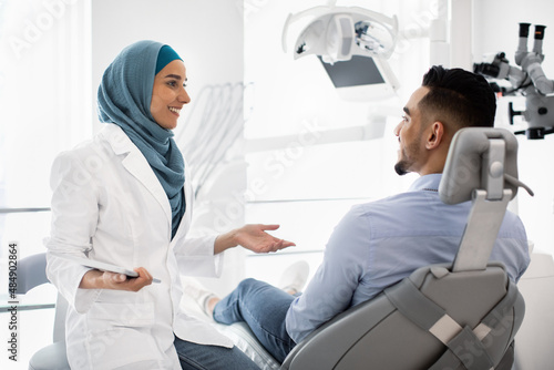Muslim Dentist Woman With Digital Tablet Consulting Male Patient About Teeth Treatment