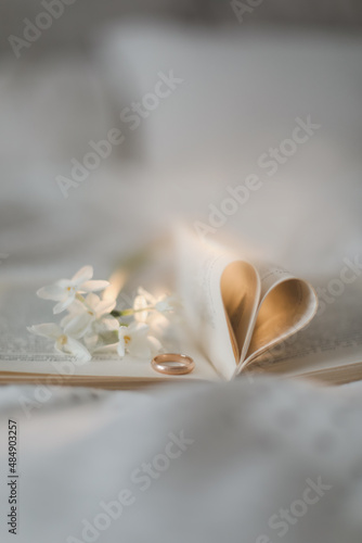Golden ring and open book with folded sheets in heart shape in bed. Wedding concept  Happy Valentine s Day