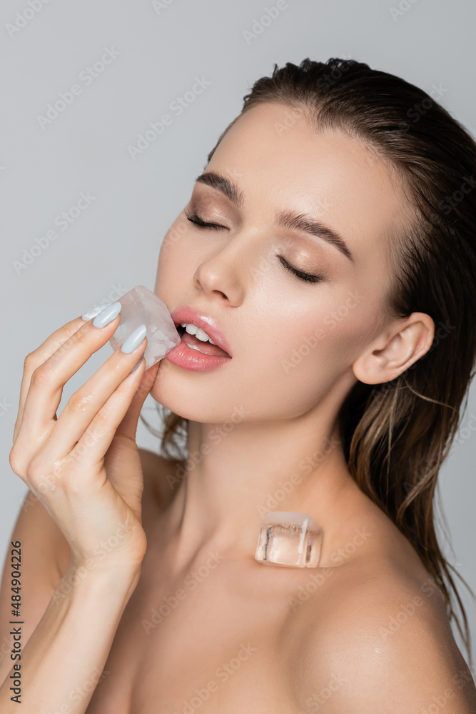 sensual woman with closed eyes holding ice cube near lips isolated on grey. sensual woman with closed eyes holding ice cube near lips isolated on grey.