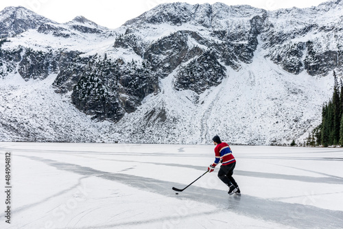 hockey player ice skating on frozen lake near snowy mountain photo