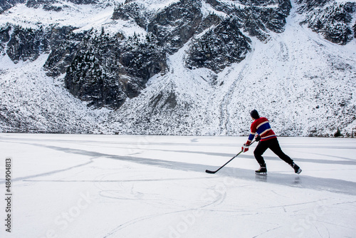 Unrecognizable hockey player ice skating on frozen lake near mountain photo