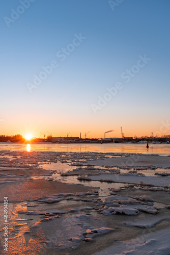 Calm winter sunset at the harbour of Riga. Partly frozen river Daugava and industrial part of the city with the Z towers in the background © Janis Eglins