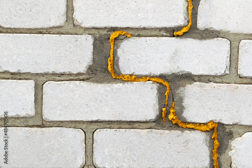 Cracked wall with filling foam. White brick wall background. Deformation of the building.