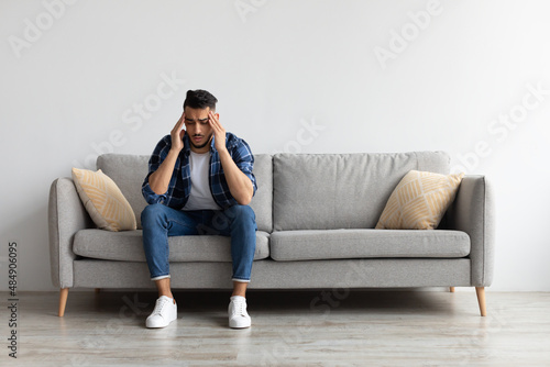 Arab man suffering from headache or migraine on couch