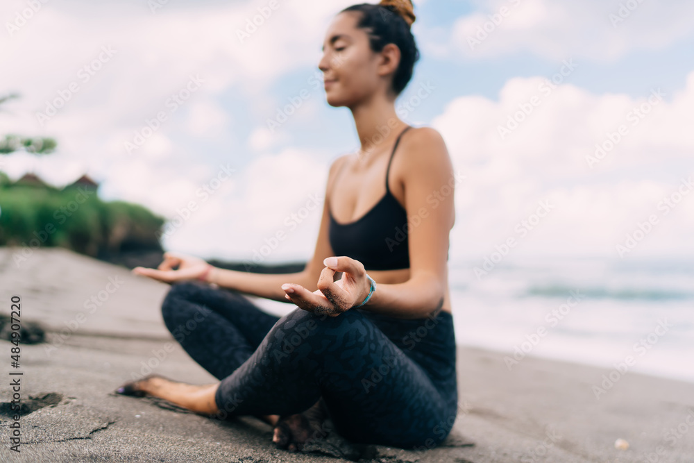 Harmony and meditation training during morning yoga at coastline beach, blurred female in sportswear sitting in lotus pose during aerobic pilates for exercising own body concentration in asana