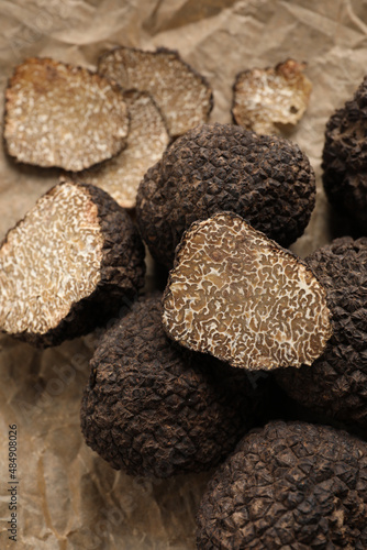 Whole and cut black truffles on parchment, closeup