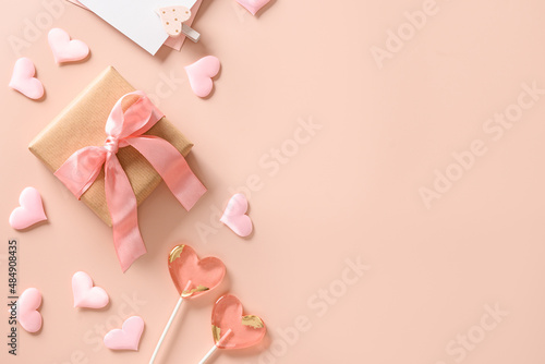 Valentine's day greeting card with gift, love letter,two sweets lollipops and pink hearts on pink background. View from above. Space for text. Flat lay.