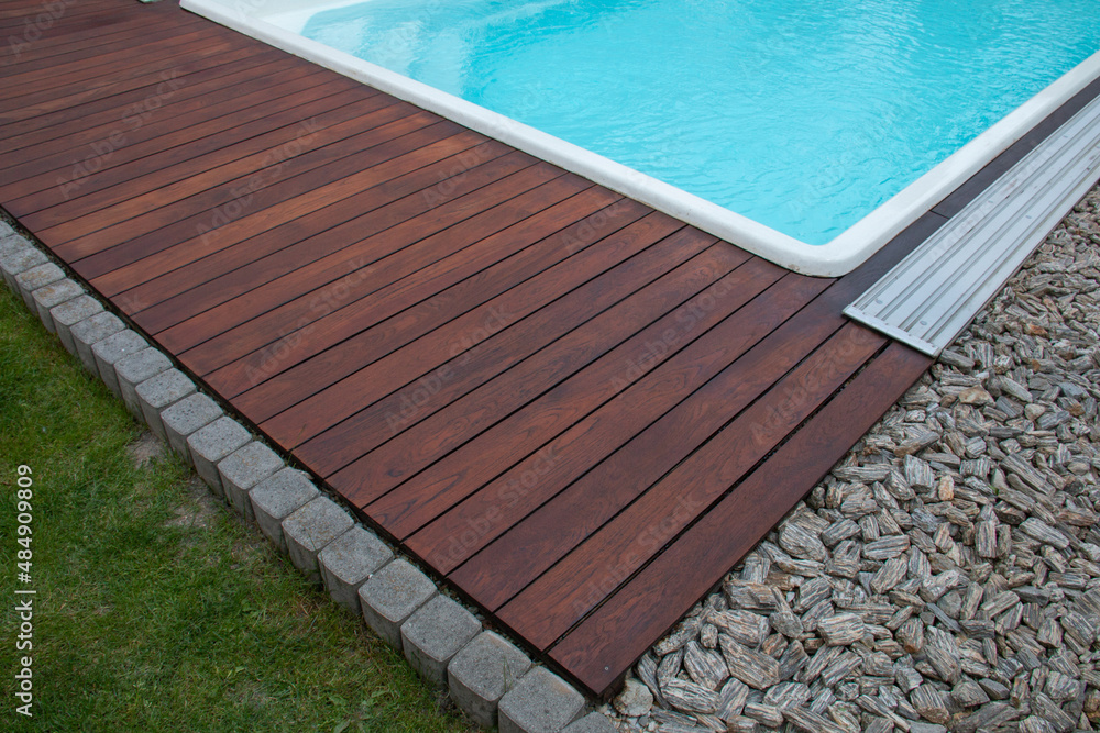 Teak wood pool deck detail next decorative stones and grass