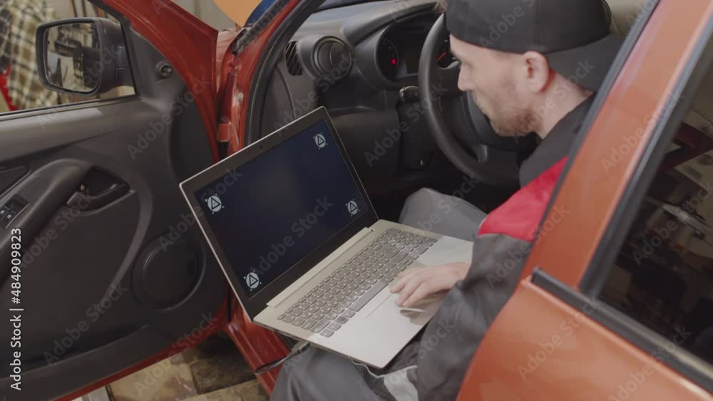 Mechanic sitting in car and doing diagnostic test on laptop while working in auto service garage Mechanic sitting in car and doing diagnostic test on laptop while working in auto service garage