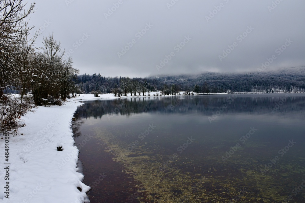 Snow covered shore of lake Bohinj in Slovenia and the mountain above shrouded in fog