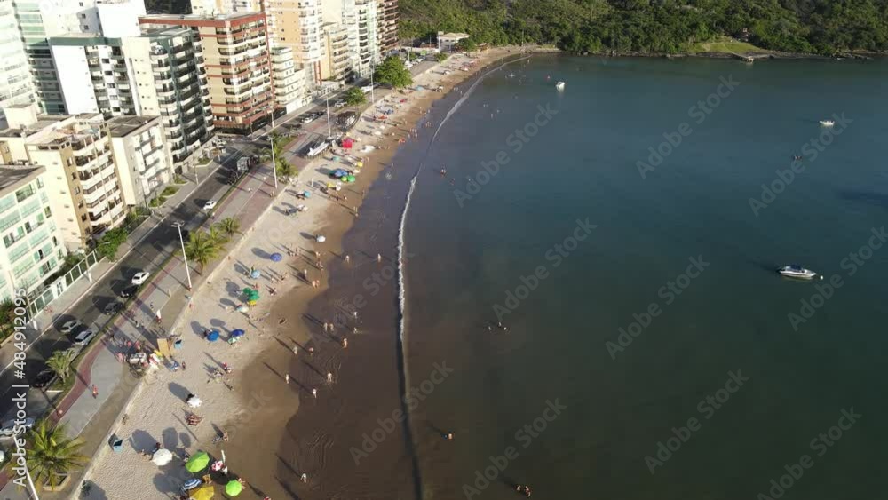 Imagem de drone da Praia do Morro em Guarapari num dia ensolarado com muitas pessoas se divertindo, aproveitando o dia na praia e praticando esportes.	