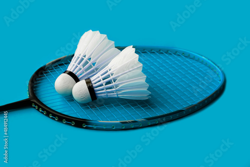 Cream white badminton shuttlecock and racket on blue floor in indoor badminton court, copy space, soft and selective focus on shuttlecocks. © Sophon_Nawit
