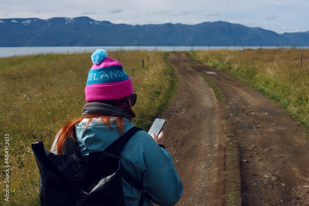 A woman loking at a mobile phone on the road in a picturesque scenery with mountains and ocean in the background