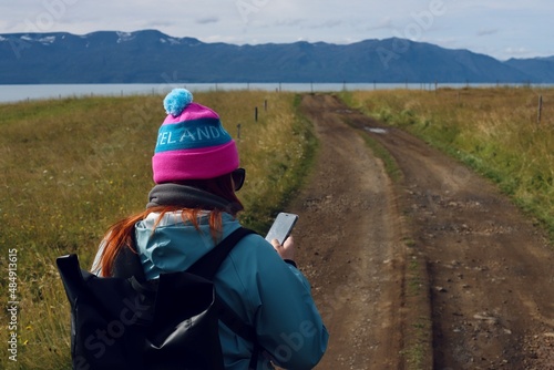 A woman loking at a mobile phone on the road in a picturesque scenery with mountains and ocean in the background