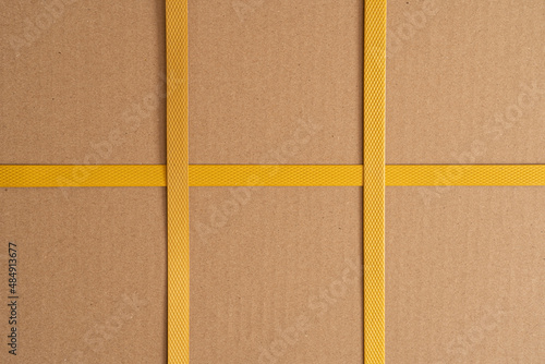 Brown cardboard box tied with yellow strapping tape. There are two crossings of the tape. Background. Texture. Form.
