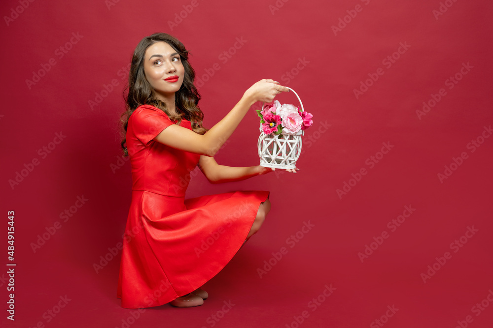 Woman looks back, smiles and holds a basket of flowers on a red b