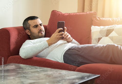 Close up photo of man usin smartphone while relaxing on comfortable sofa. Modern house concept. photo