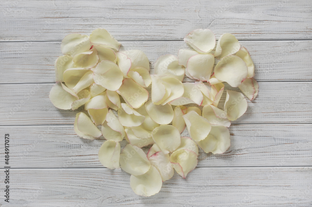 White heart made of rose petals. Heart on a wooden light background. Background for Valentine's Day. The concept of love.