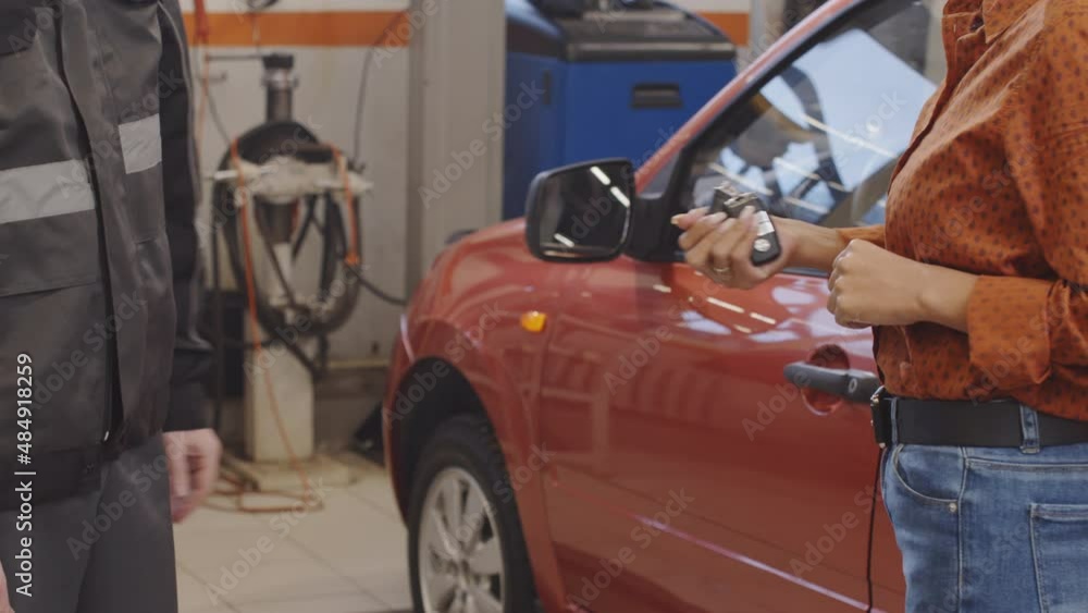 Midsection shot of auto mechanic giving car key to female client after servicing in repair shop Midsection shot of auto mechanic giving car key to female client after servicing in repair shop