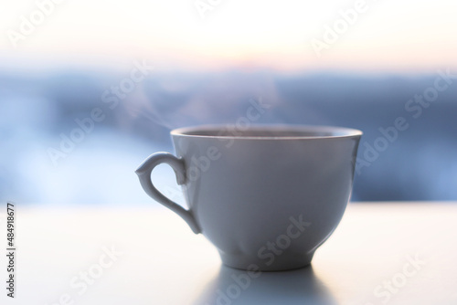 Hot coffee cup with smoke on sunrise background. Fresh start in the morning, view from the window with cozy atmosphere