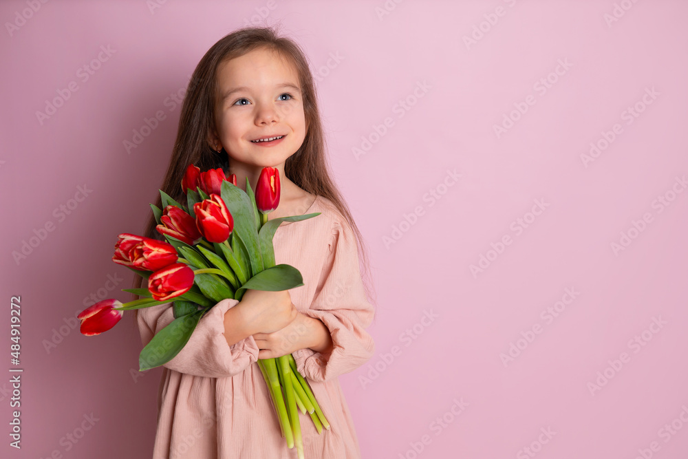 A little cute girl holding a bouquet of tulips Pink background. Happy women's day. Space for text. Bright Emotions. A little cute girl holding a bouquet of tulips Pink background. Happy women's day. Space for text. Bright Emotions.