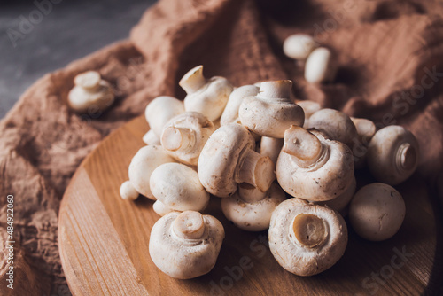 Fresh white champignons on a cutting board on a brown textile background. Kitchen, cooking, recipes. Mushrooms, ingredient