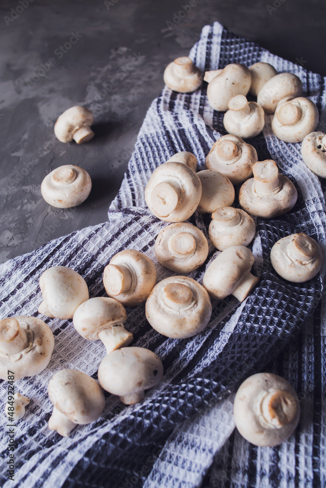 Fresh white champignons on a kitchen towel on a gray background. Kitchen, cooking, recipes. Mushrooms, ingredient.