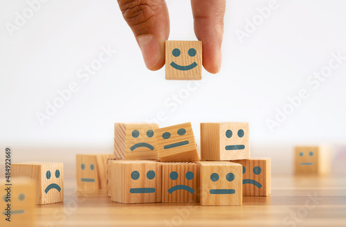 Hand picking smiling face wooden cube. Symbol of costumer service review. Concept of advantages and benefits of smiling face in business.