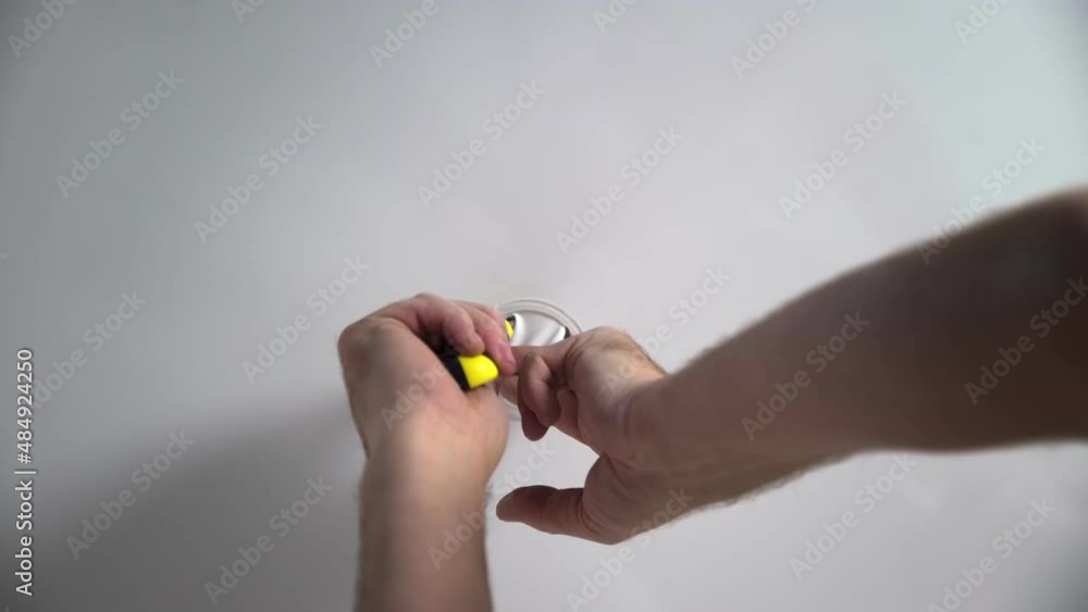 A close-up of an unrecognizable male electrician cutting a hole for a future lamp. Installation of lighting fixtures, wiring under the ceiling.