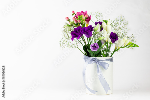 Different colors beautiful flowers bouquet in vintage white vase with ribbon on white background.