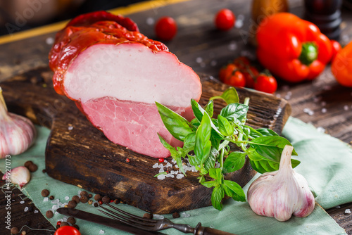 Meat balyk or boiled pork, beef and bacon, whole or piece cut on a kitchen cutting board, spices and vegetables, dark and moody, clouseup on a black wooden isolated background, top photo