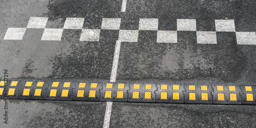 speed bump of black and yellow colours located on grey asphalt road at white marking under bright light close upper view