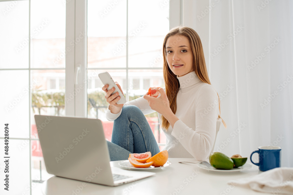Young beautiful woman working with laptop at home in front of a large window with morning light Young beautiful woman working with laptop at home in front of a large window with morning light