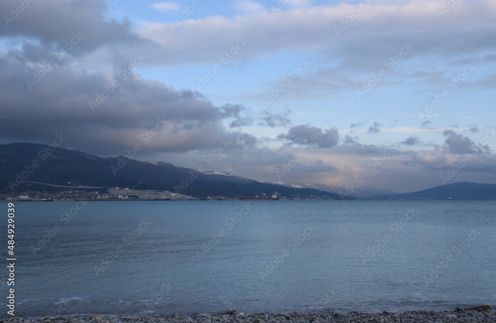 The snowy mountain peaks of the Black Sea coast at the foot of the port city are shrouded in fluffy clouds at sunset.