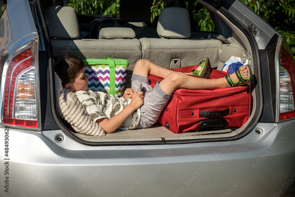 Cute little boy laying on the back of the bags and baggage in the car