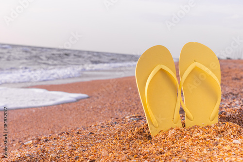 Summer background of the beach and yellow shoes on the sand. Free space for your decoration. The concept of relaxation and long-awaited vacation. Copyspace
