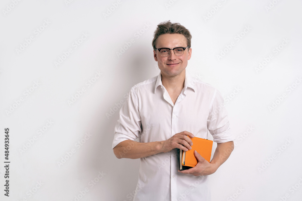 Businessman in eye glasses wearing white shirt holding orange notebook or journal isolated on white background or in the office. Portrait of a positive young businessman holding his diary. Businessman in eye glasses wearing white shirt holding orange notebook or journal isolated on white background or in the office. Portrait of a positive young businessman holding his diary.