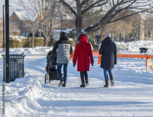 Three women walking down a snow covered path in an urban park, baby stroller, daytime,