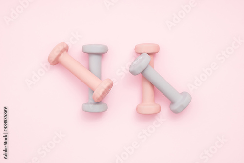 Four pastel color exercise weights on pastel pink background with soft shadow. Exercise, healty lifestyle or New Year resolution concept. Flat lay.