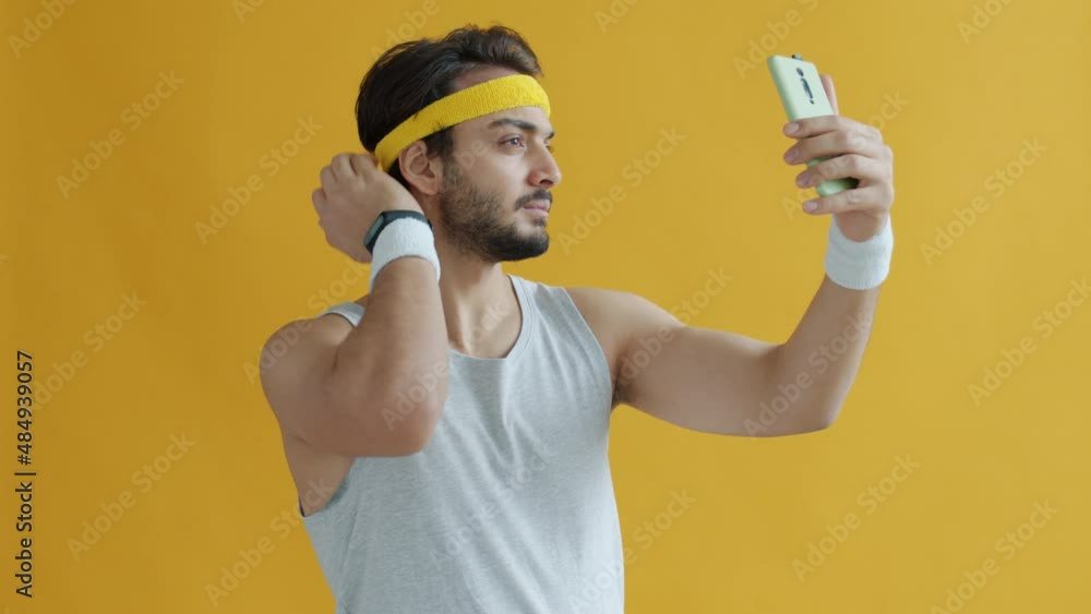 Slow motion portrait of handsome Arab bodybuilder posing for smart phone camera taking selfie on yellow background. Sportsman and modern technology concept. Slow motion portrait of handsome Arab bodybuilder posing for smart phone camera taking selfie on yellow background. Sportsman and modern technology concept.