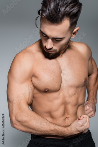 bearded and muscular sportsman looking muscles isolated on grey.